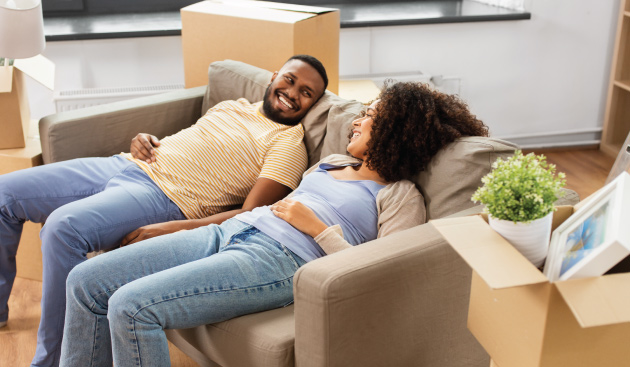 young couple moving into new house, resting on couch smiling and looking at each other
