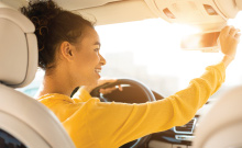 young new driver smiling as she adjusts her rear-view mirror in her new car